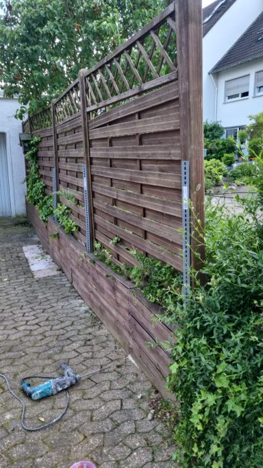 Holzsichtschutzzaun mit Lattice und Pflanzen im Garten auf einem gepflasterten Weg.